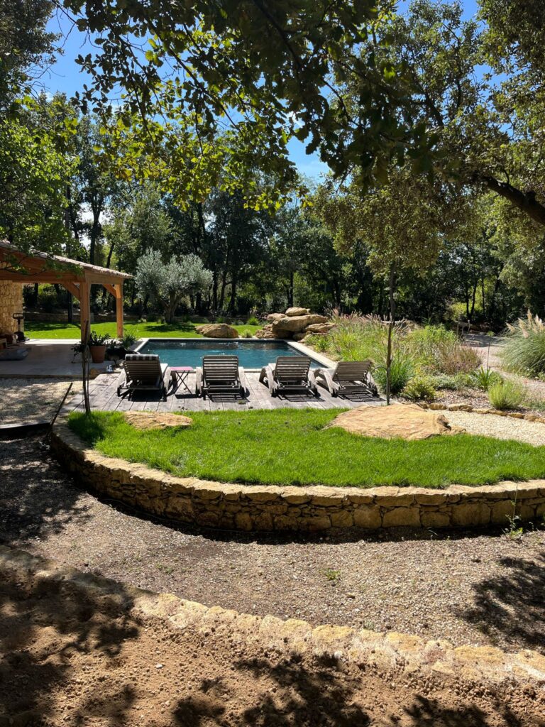 Aménagement paysager avec gazon naturel, terrasse en bois et plantations autour d'une piscine
