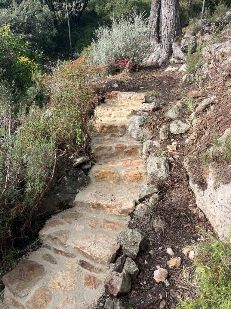 Escalier paysager en pierres naturelles aménagé sur un talus de jardin entouré de végétation méditerranéenne.